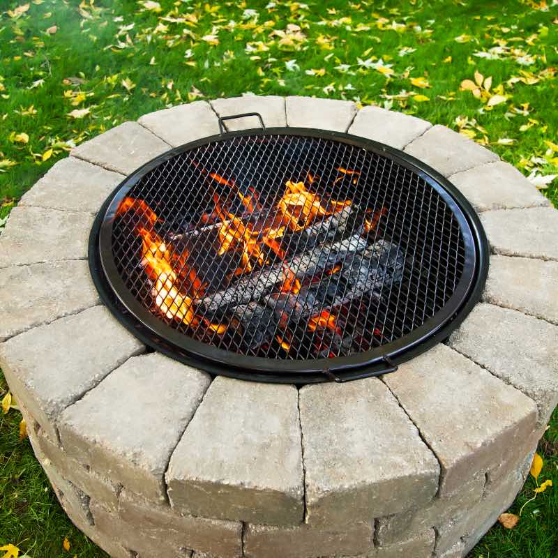 Fire roaring in fire pit with round grilling grate placed over to create a grill.