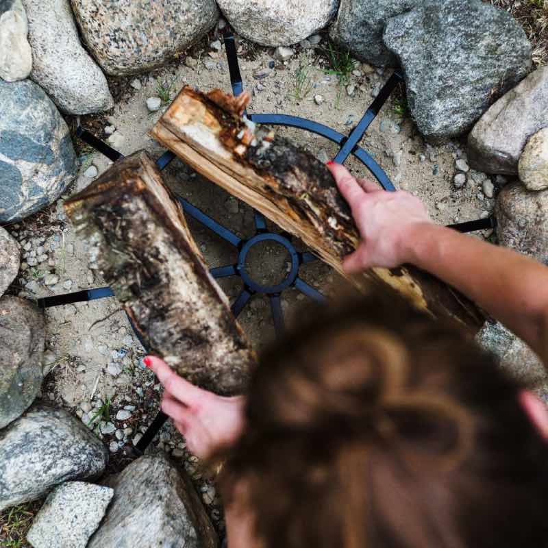 place firewood on top of round fire grate with upward-angled spokes