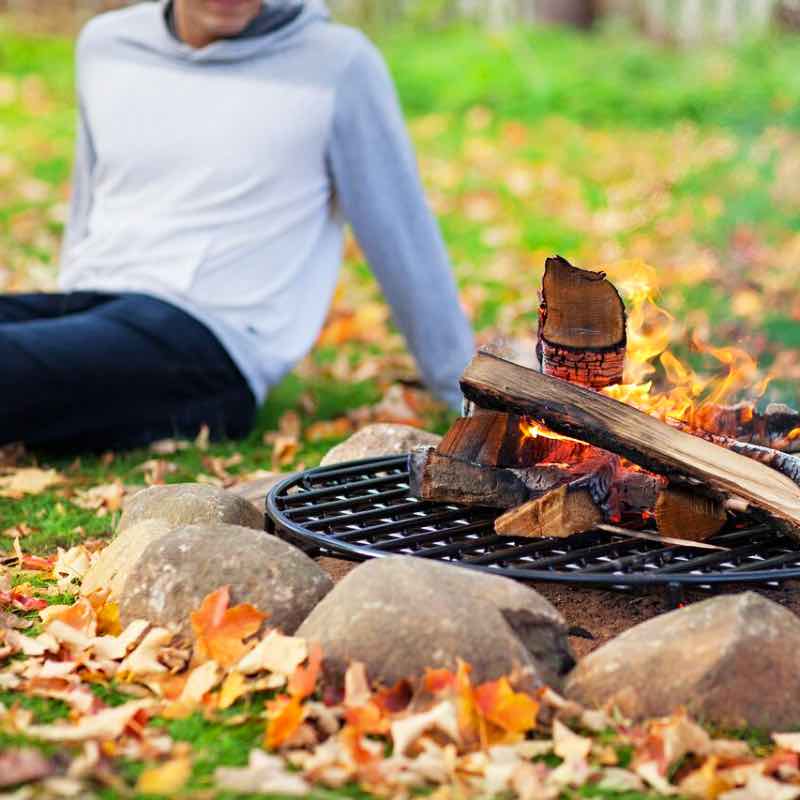 Man sitting by the fire burning elevated by four inch tall steel fire pit grate in fire pit.
