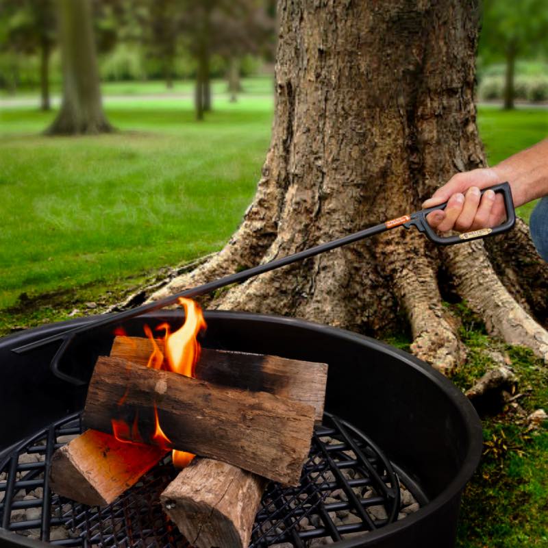 Man's hand poking and rearranging logs inside a fire pit ring with Walden fire poker