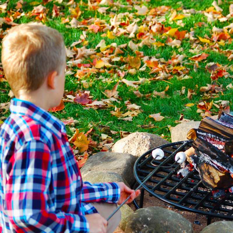 kid using stainless steel roasting stick with marshmallows on the end over embers of a fire