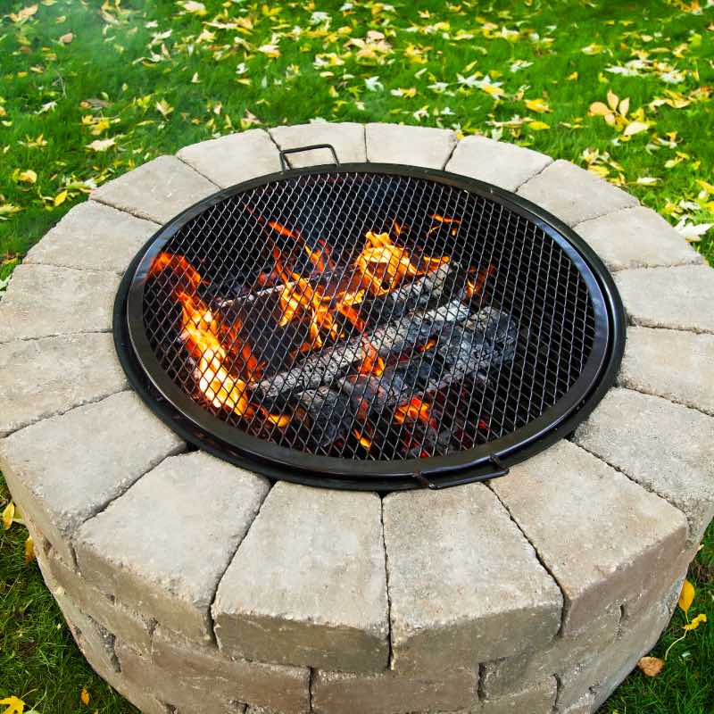 Fire roaring in fire pit with round grilling grate placed over to create a grill.