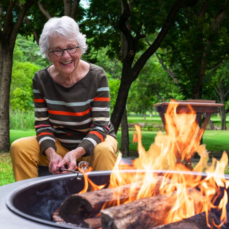 Happy grandmother roasting marshmallows over roaring fire in Legacy Fire Pit