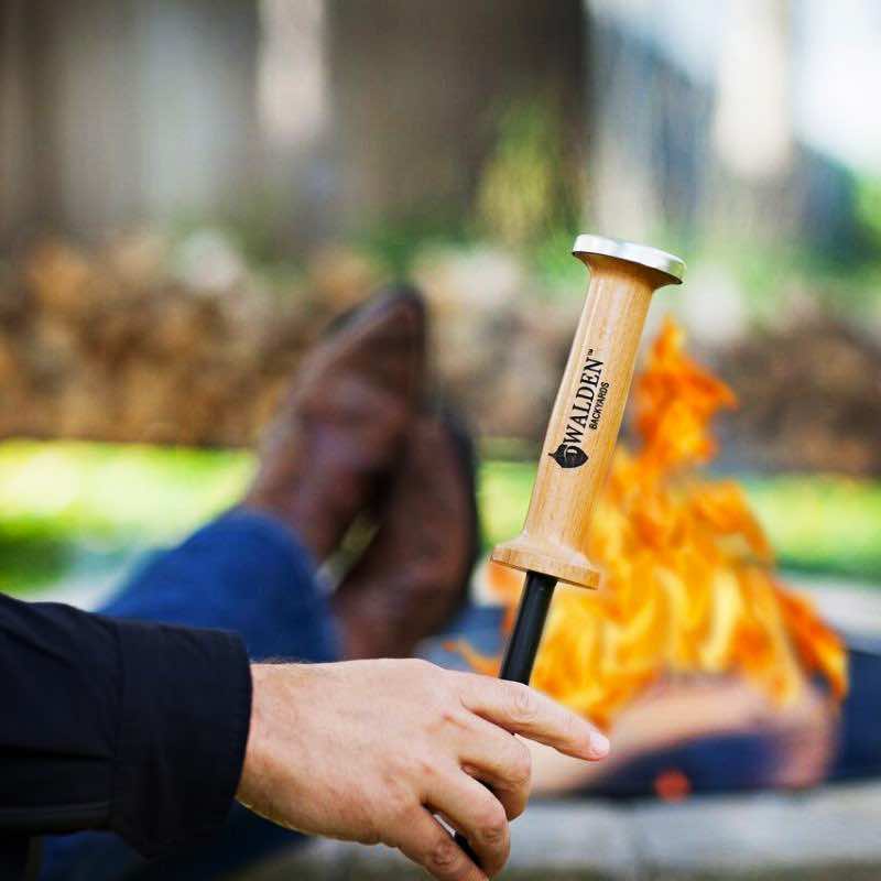 Man sitting by outdoor fire pit holding Walden blow through stoker poker 
