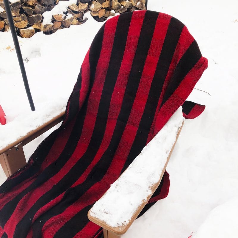 Fire retardant, warm wool blanket from Walden Backyards spread out on a fireside chair covered in snow to create a cozy fireside seat.