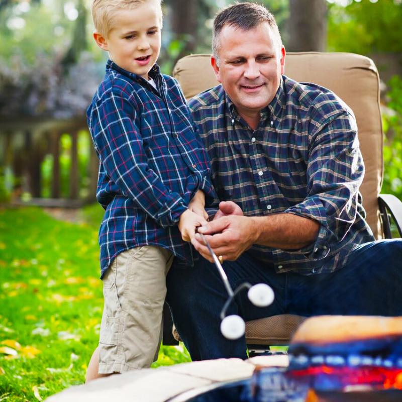 father and son roasting marshmallows using long extended roasting sticks.